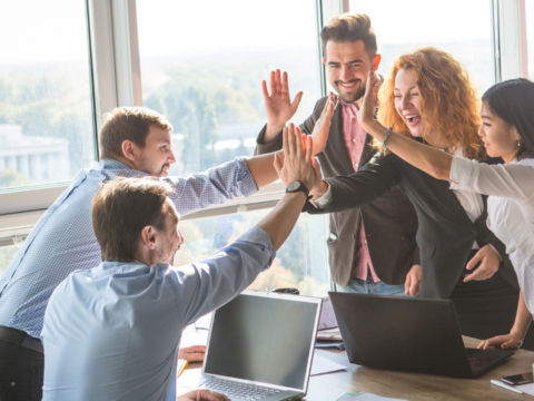 A team in an office celebrate by high fiving one another.